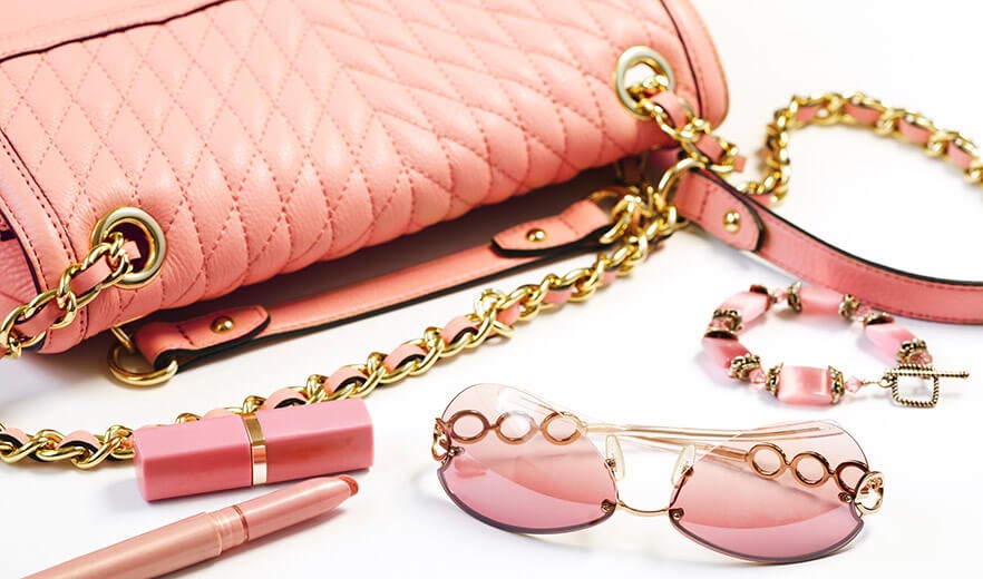 Eine Tasche, Sonnenbrille und weitere rosafarbene Accessoires für Frauen verteilt auf einem weißen Hintergrund